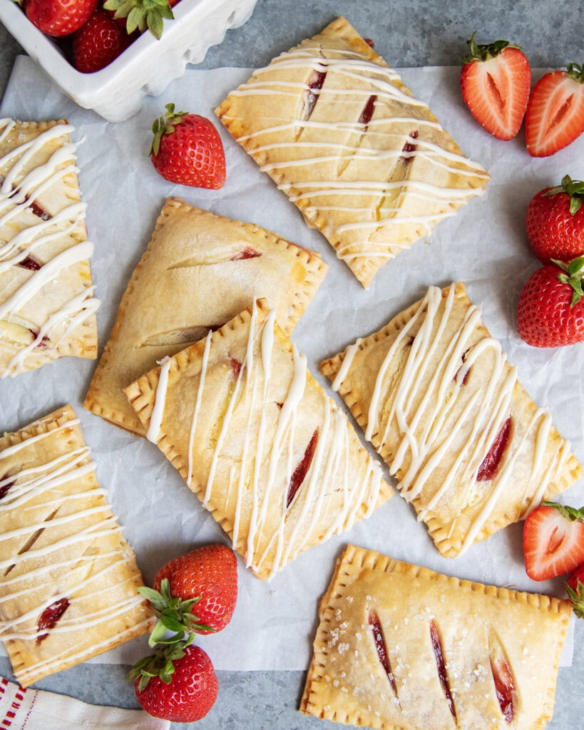 An above view of strawberry hand pies, some are drizzled with vanilla icing.