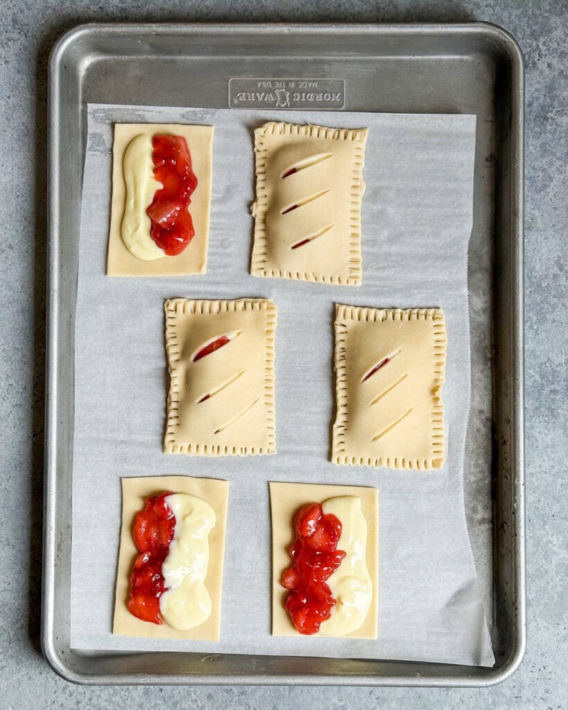 Strawberry cheesecake hand pies on a tray, half are uncovered showing the cheesecake and strawberry filling.