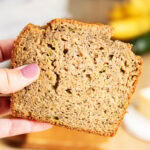 A hand holding a piece of banana zucchini bread.