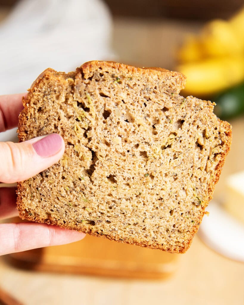 A hand holding a piece of banana zucchini bread. 
