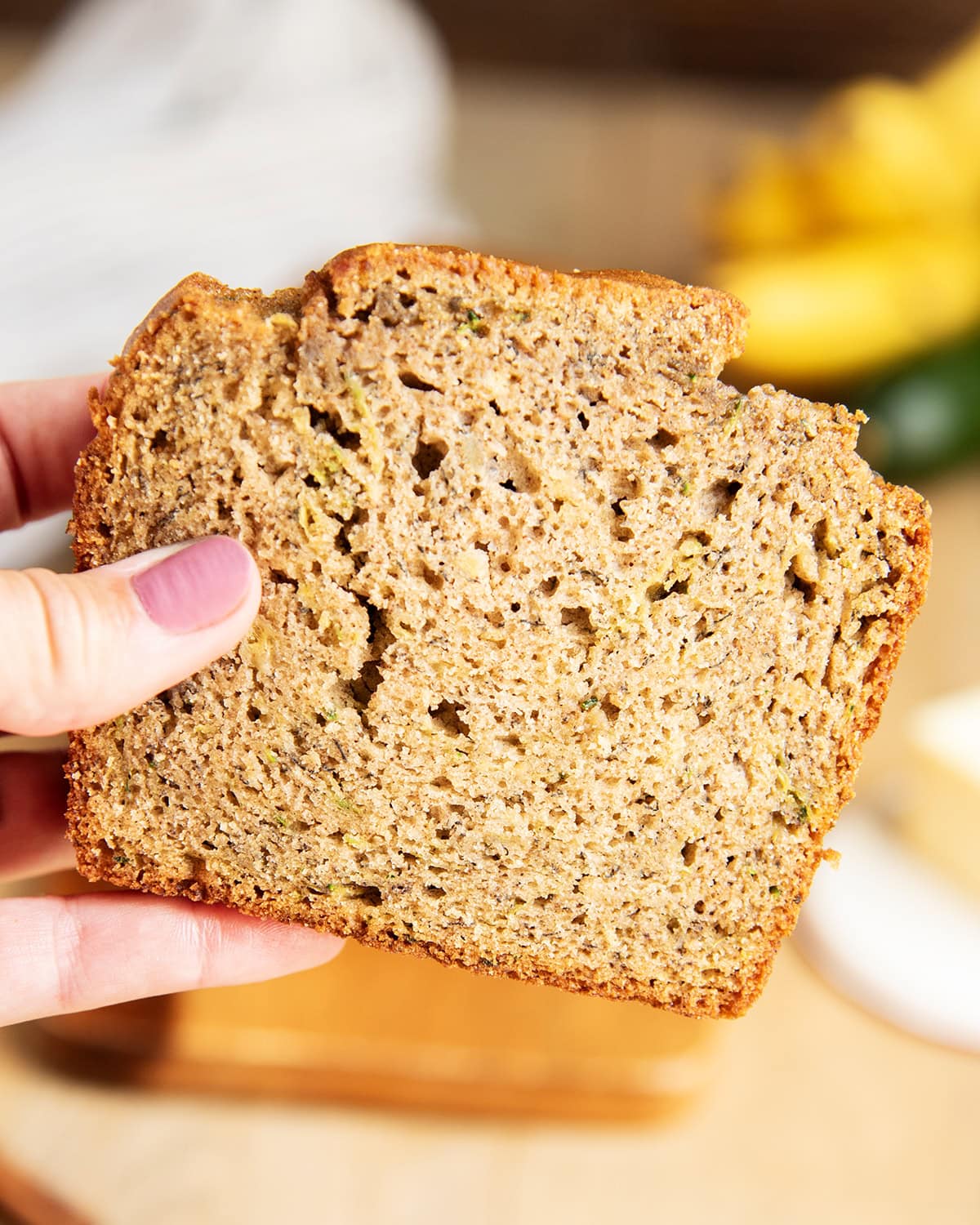 A hand holding a piece of banana zucchini bread.