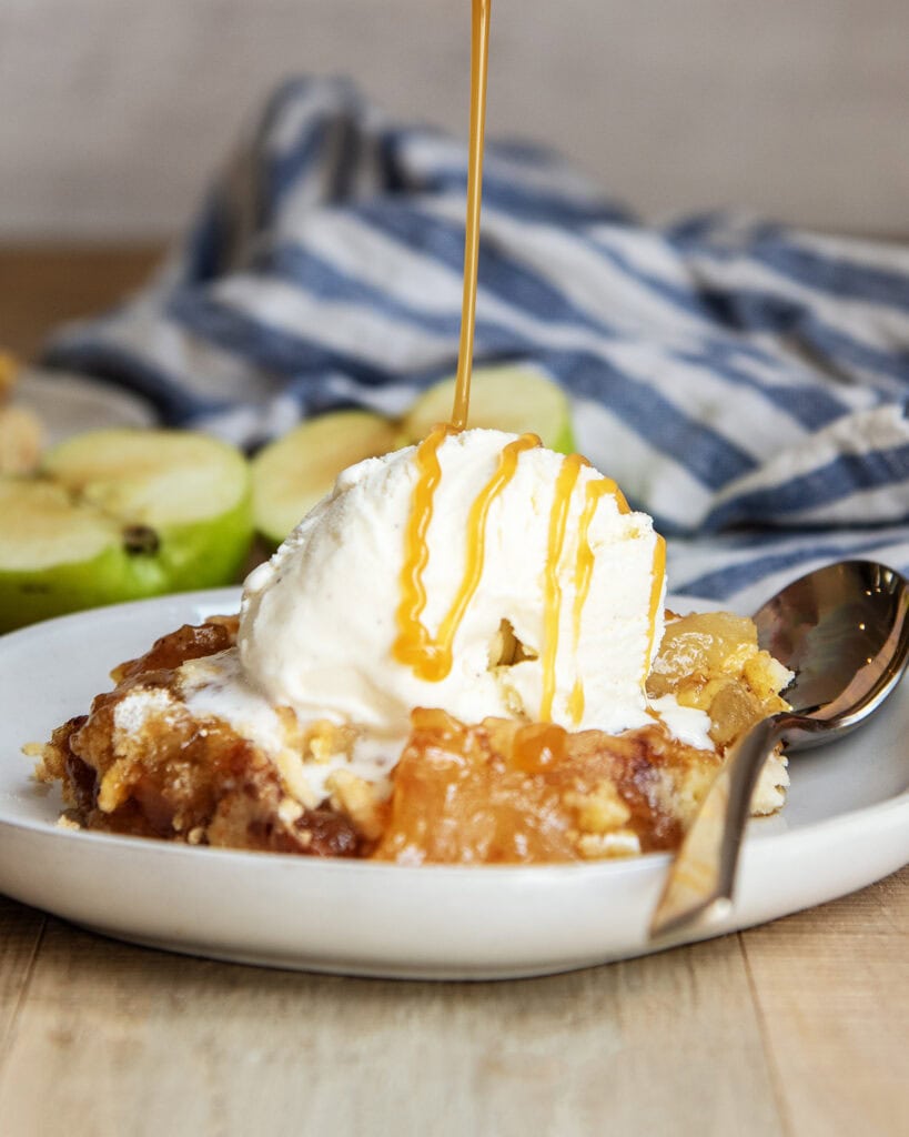 Caramel syrup being poured over a scoop of vanilla ice cream on apple cobbler. 