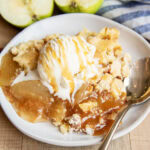 A plate of apple dump cake topped with vanilla ice cream and caramel syrup.