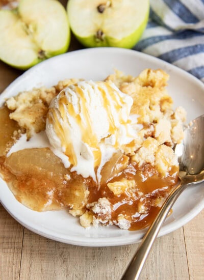 A plate of apple dump cake topped with vanilla ice cream and caramel syrup.