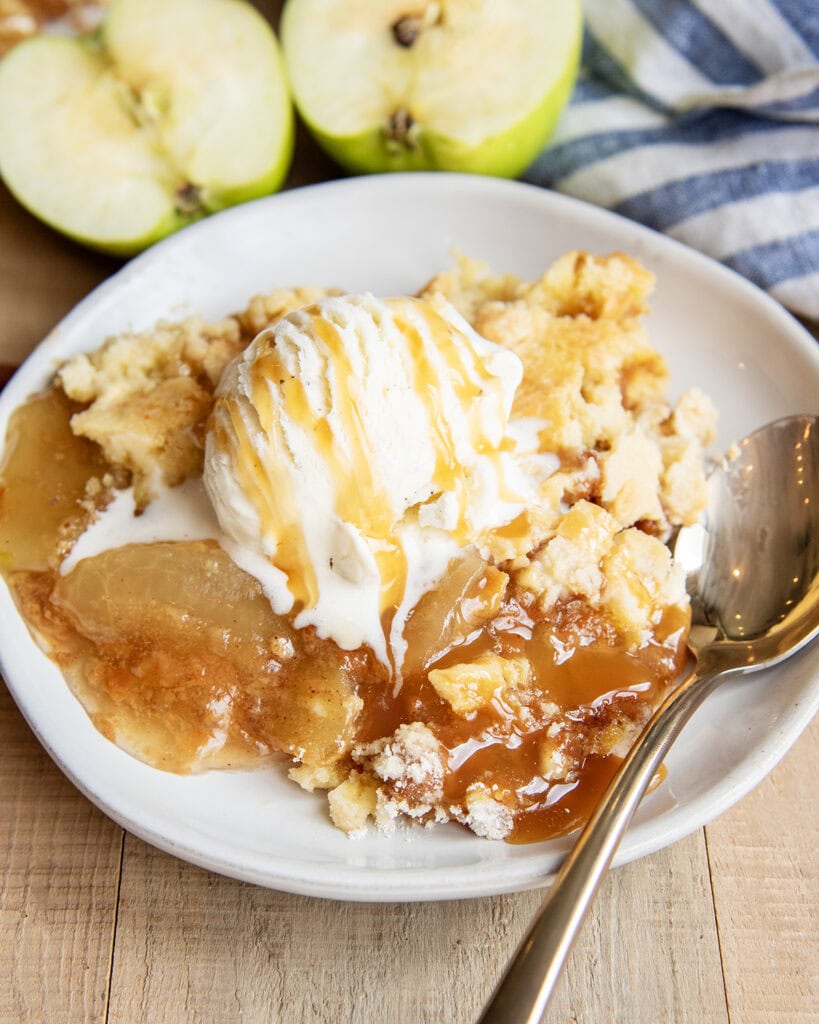 A plate of apple dump cake topped with vanilla ice cream and caramel syrup. 