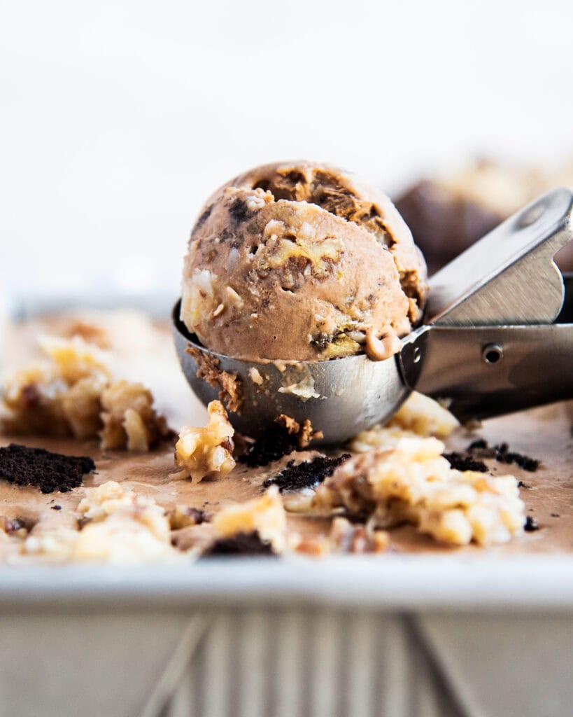A scoop of chocolate ice cream full of chocolate cake pieces, and coconut pecan frosting.