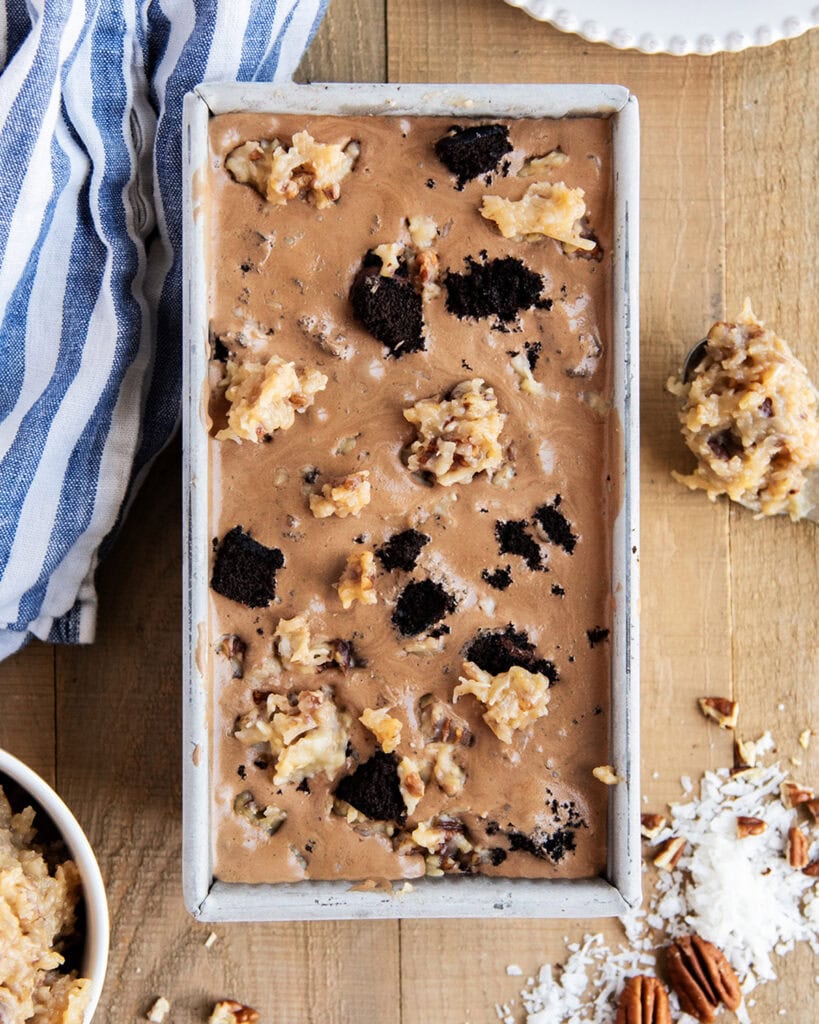 An above view of a bread pan full of German chocolate cake ice cream, with chocolate cake pieces, and dollops of coconut pecan frosting.