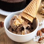 A bowl of German Chocolate Ice Cream topped with a scoop of coconut pecan frosting, and two ice cream cones.