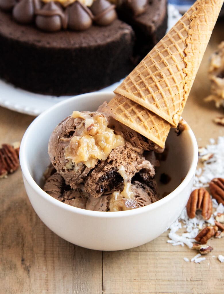 A bowl of German Chocolate Ice Cream topped with a scoop of coconut pecan frosting, and two ice cream cones.