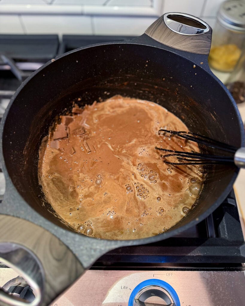 A bowl of chocolate custard cooking on the stove, with chocolate pieces melting into it.