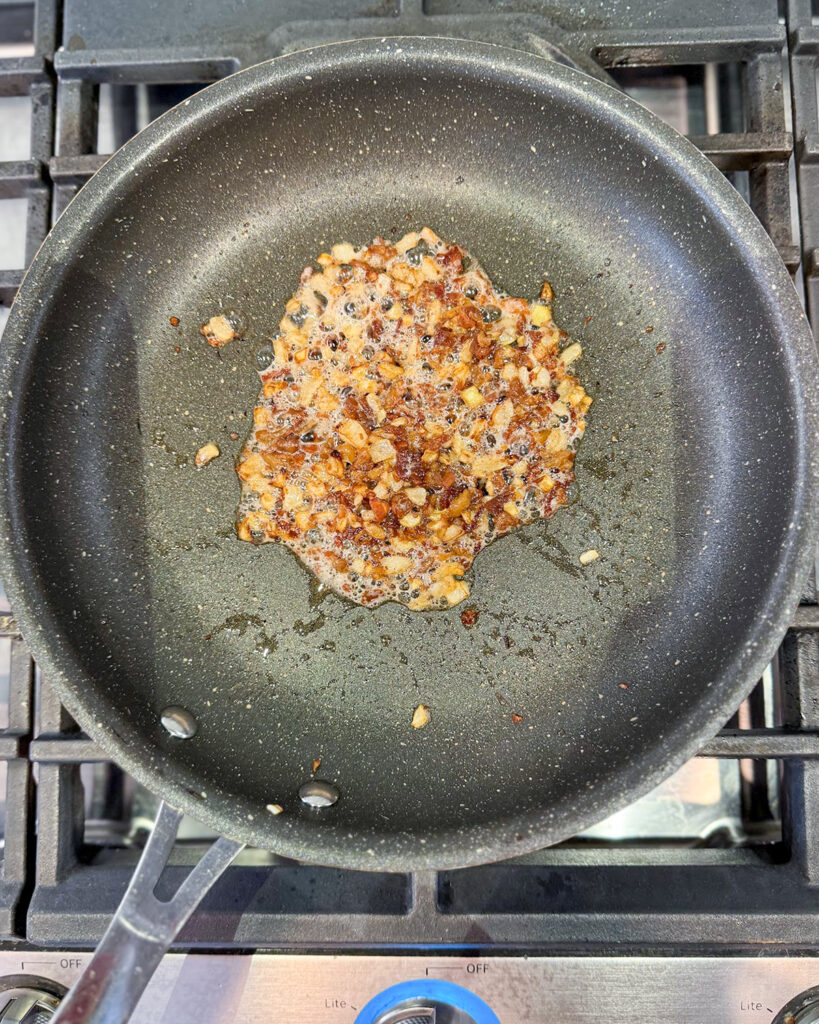 Sauteed onion and bacon bits in a skillet.