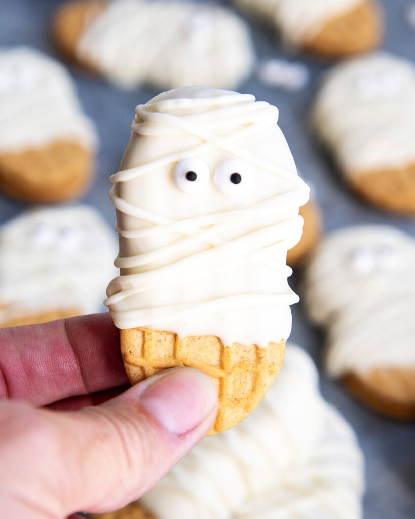 A hand holding a Nutter Butter dipped in white chocolate and decorated to look like a mummy.