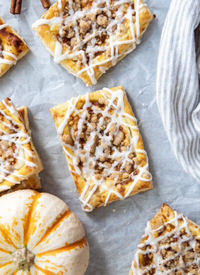 An above view of pumkin cream cheese danishes stopped with a crumb topping and vanilla icing.