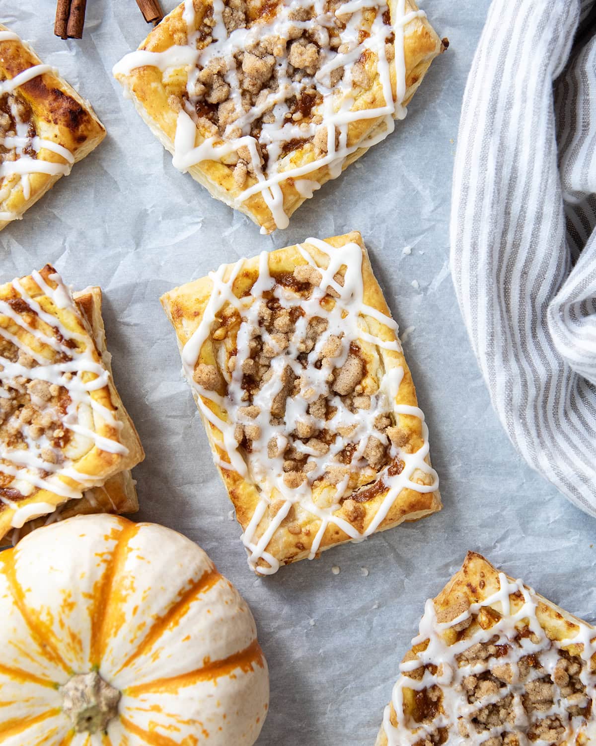 An above view of pumkin cream cheese danishes stopped with a crumb topping and vanilla icing.