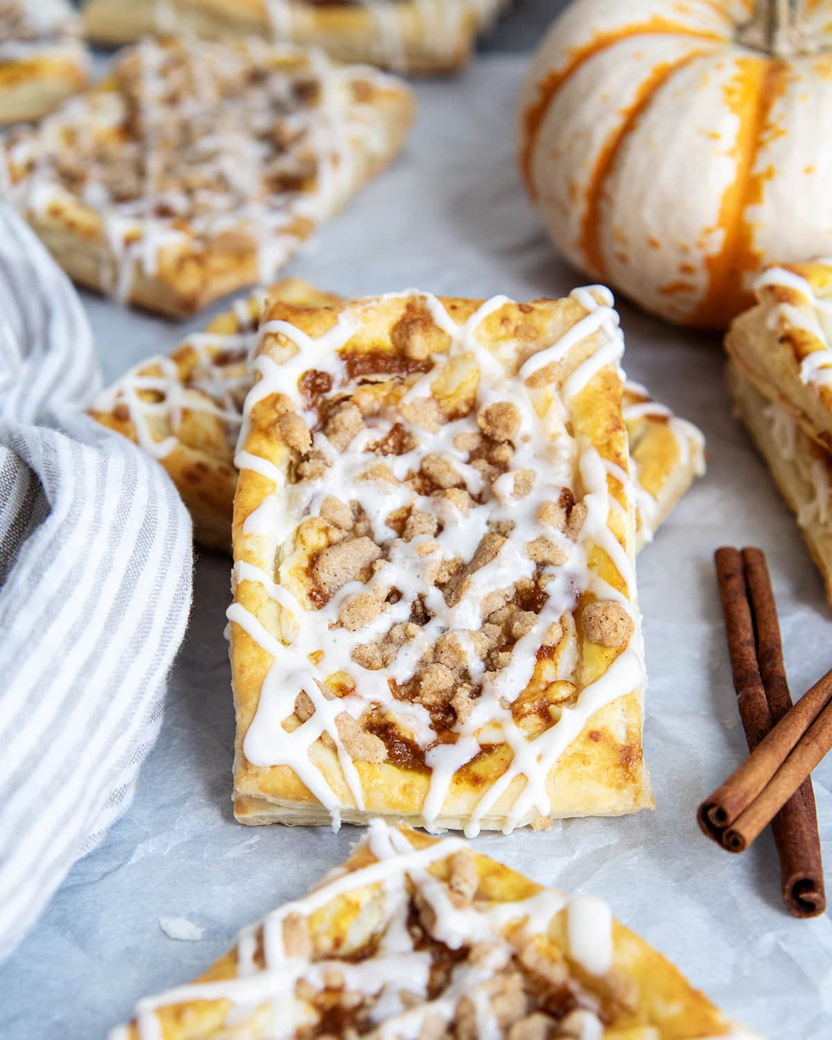 A pumpkin danish laying on another danish on a piece of parchment paper.