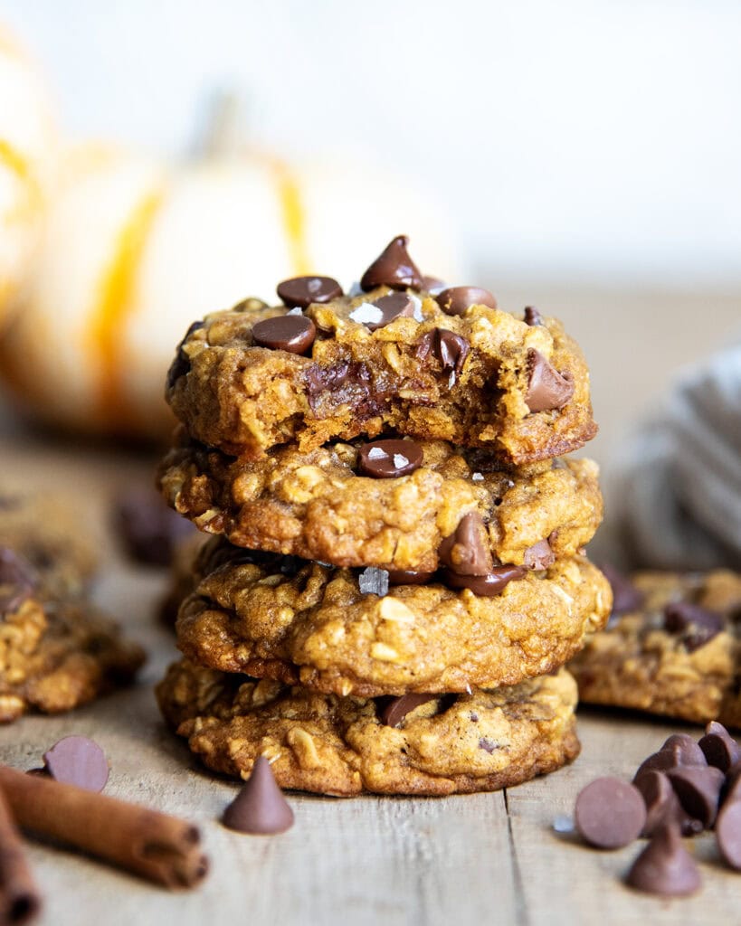 A stack of four pumpkin oatmeal chocolate chip cookies. The top has a bite out of it.