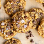 A pile of pumpkin oatmeal chocolaet chip cookies on a wooden table.