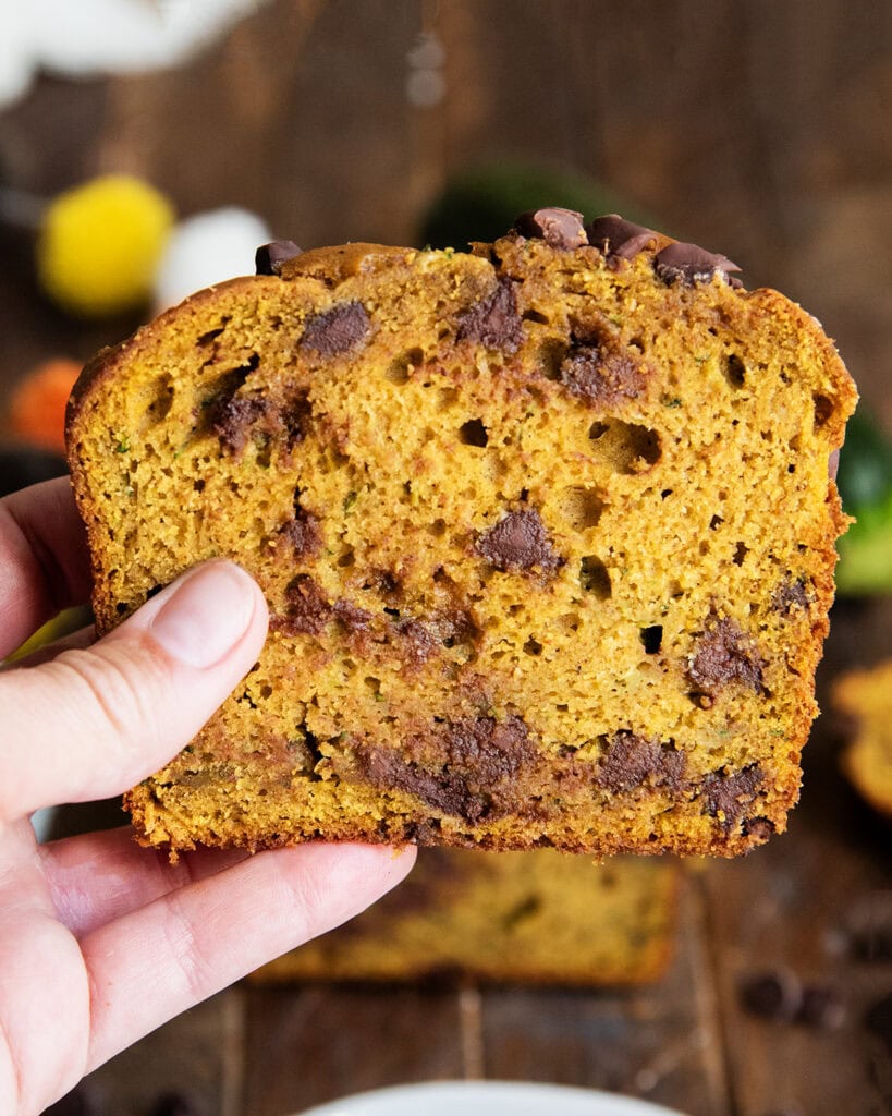 A hand holding a piece of pumpkin zucchini bread with chocolate chips