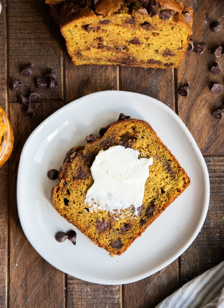 A slice of zucchini pumpkin bread on a plate slathered with butter.