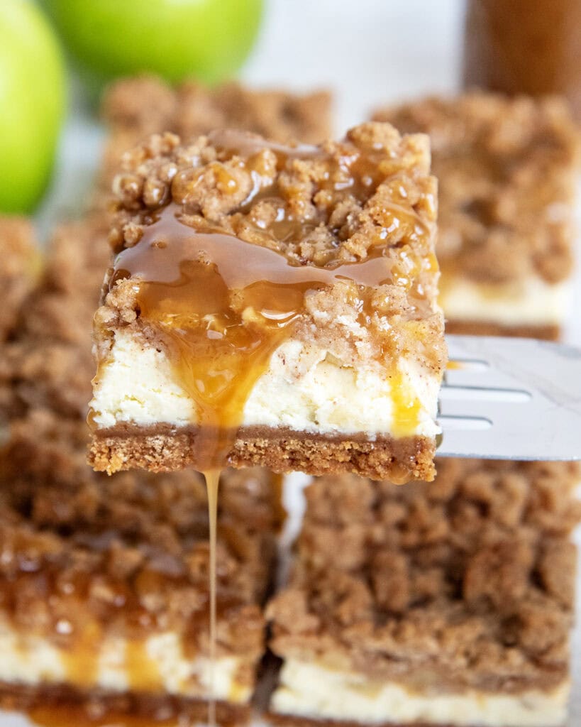Caramel Apple Cheesecake Bars with caramel sauce drizzling over the side on a spatula.