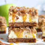 A stack of two caramel apple cheesecake bars with a crumb topping.