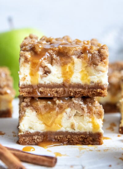 A stack of two caramel apple cheesecake bars with a crumb topping.