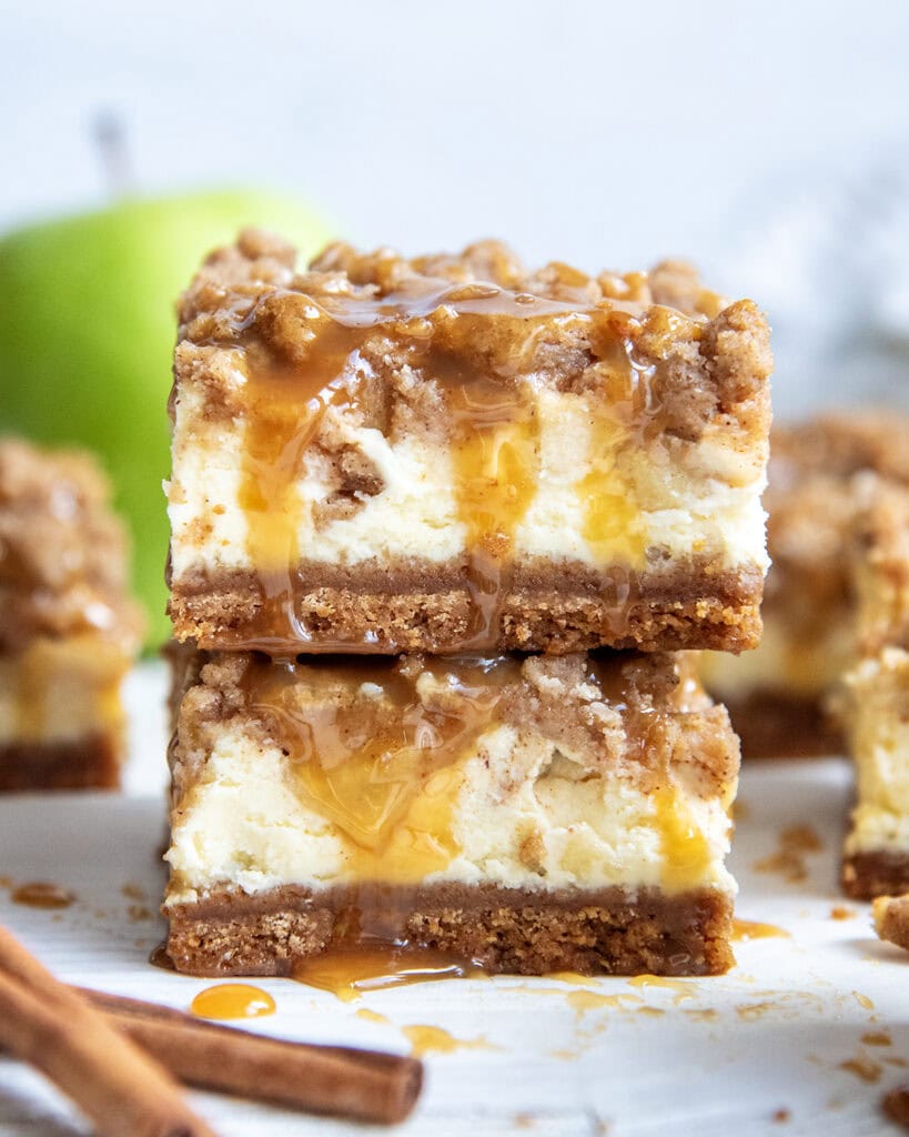 A stack of two caramel apple cheesecake bars with a crumb topping. 