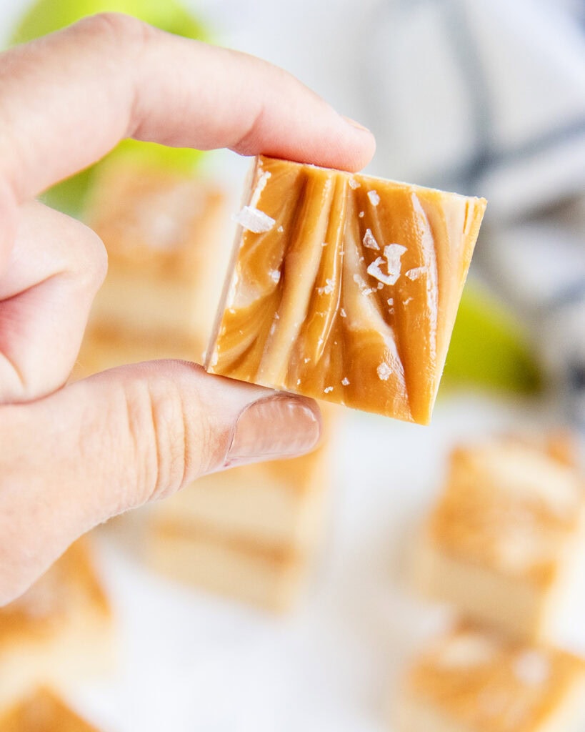 A hand holding a piece of caramel apple fudge, showing the caramel swirls on top.