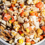 A bowl full of a halloween snack mix with popcorn, peanuts, chex, and reeses pieces.