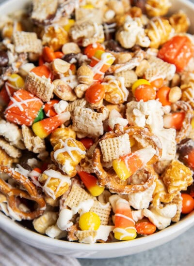 A bowl full of a halloween snack mix with popcorn, peanuts, chex, and reeses pieces.