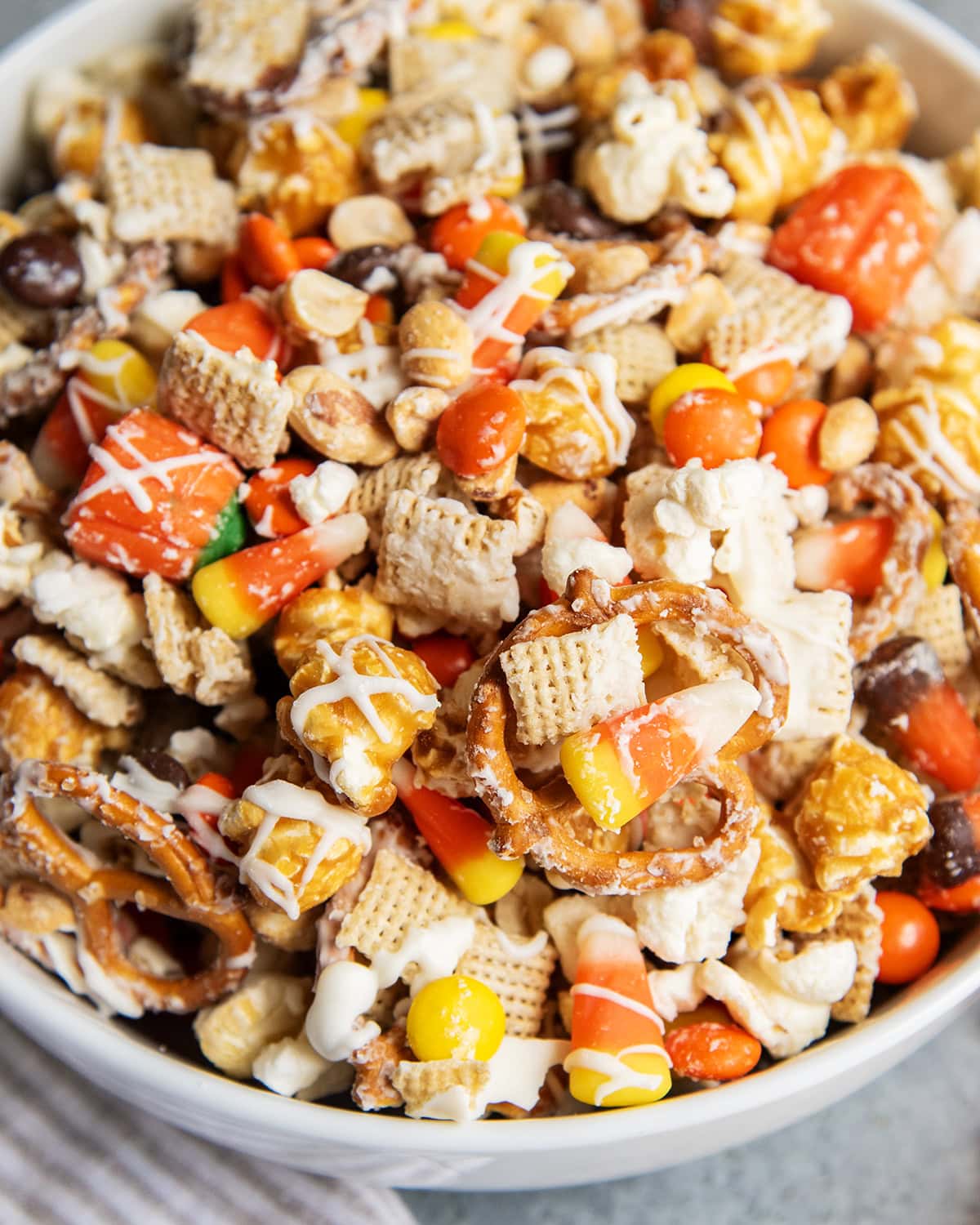 A bowl full of a halloween snack mix with popcorn, peanuts, chex, and reeses pieces.