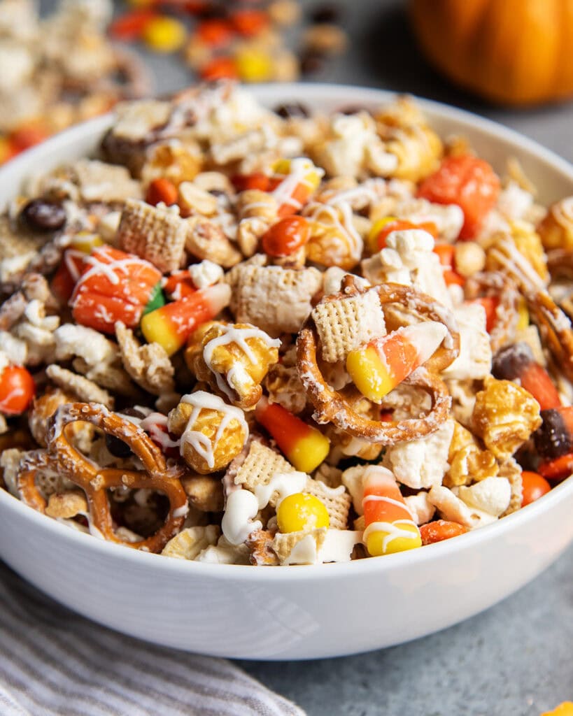 A bowl full of a halloween snack mix with popcorn, peanuts, chex, and reeses pieces.