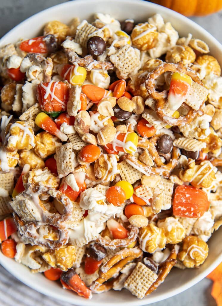 A bowl full of a halloween snack mix with popcorn, peanuts, chex, and reeses pieces.