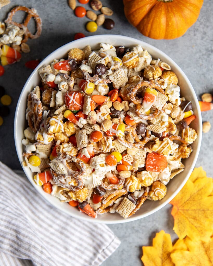A bowl full of a halloween snack mix with popcorn, peanuts, chex, and reeses pieces.