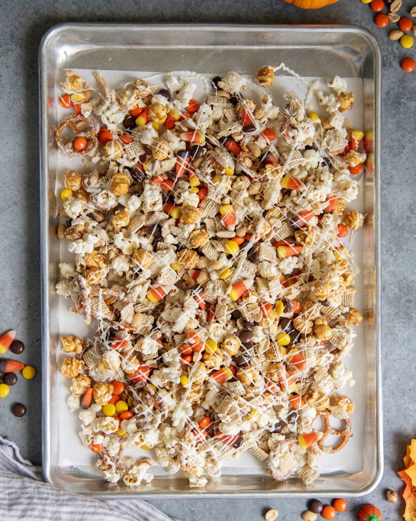 An above view of a pan of a halloween snack mix, with white chocolate coated chex and popcorn, and reeses pieces and candy corn.