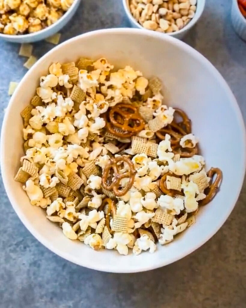 A bowl of popcorn, chex, and pretzels. 
