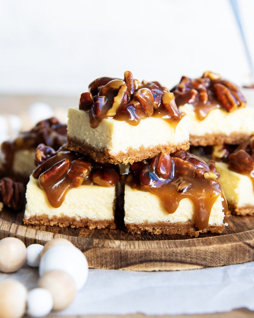 A pile of pecan pie cheesecake bars on a wooden board.