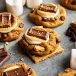 A pumpkin smore cookie on a graham cracker square. Its topped with a golden marshmallow and a Hershey square.