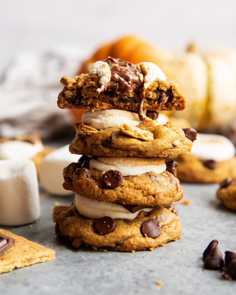 A stack of four pumpkin chocolate chip marshmallow cookies, the top is broken in half showing the inside of the cookie.