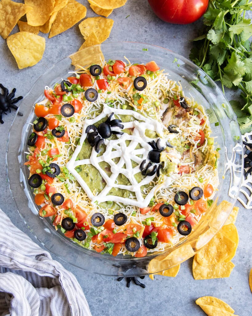 An above view of seven layer dip with a spider web design of sour cream and olive "spiders" on top.