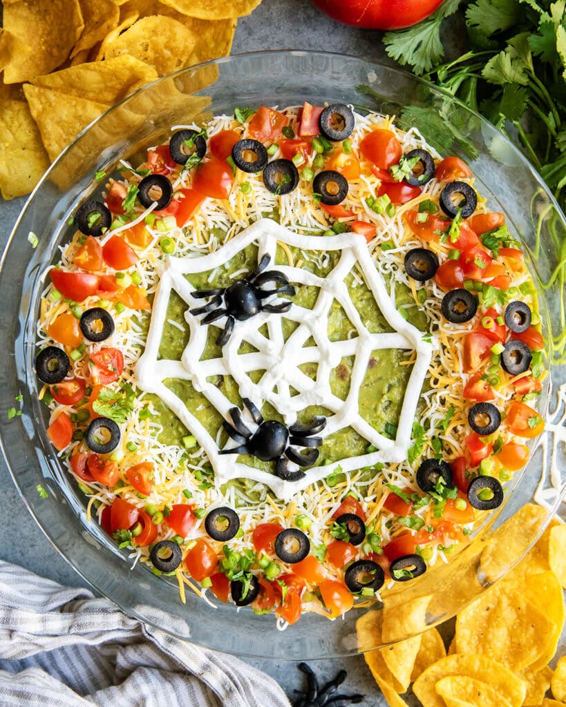 An above view of seven layer dip with a spider web design of sour cream and olive "spiders" on top.