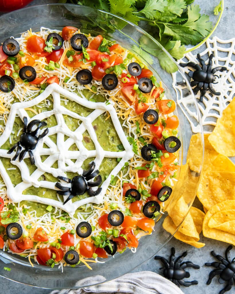 An above view of seven layer dip with a spider web design of sour cream and olive "spiders" on top.