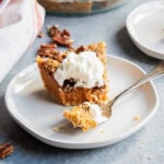 A slice of sweet potato pie on a plate with a fork of the pie in front of the slice.