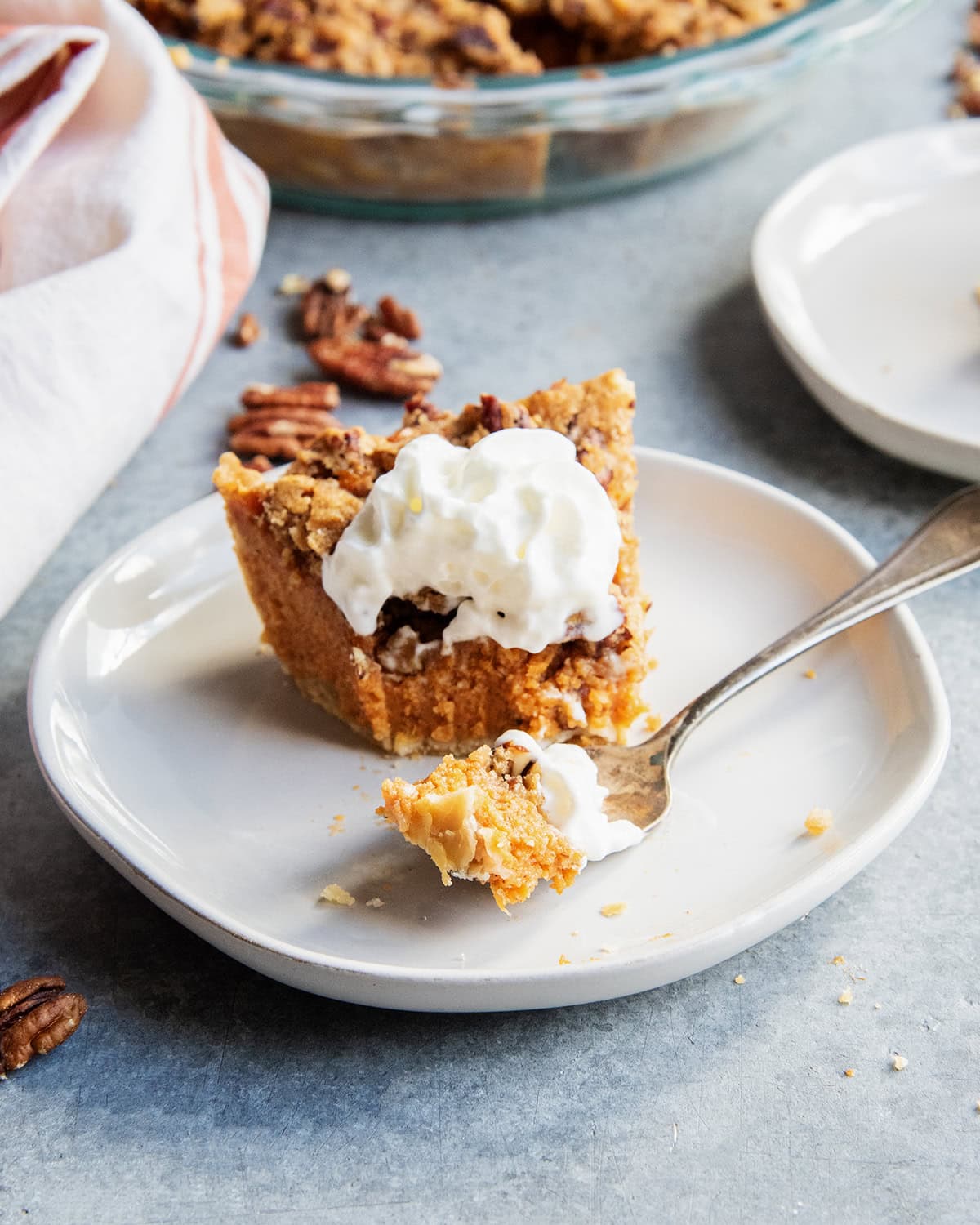 A slice of sweet potato pie on a plate with a fork of the pie in front of the slice.