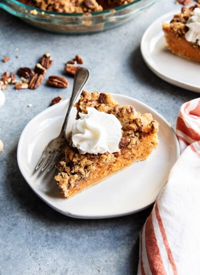 A slice of sweet potato pie with pecan topping on a plate with whipped cream on top.