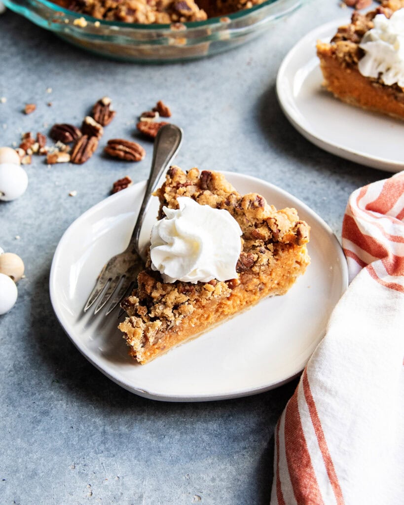 A slice of sweet potato pie with pecan topping on a plate with whipped cream on top.