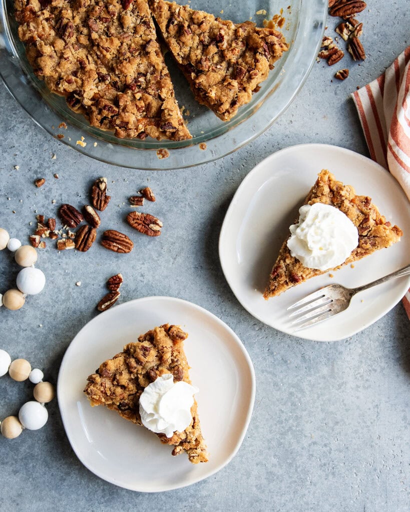 An above view of two slices of sweet potato pie next to the whole pie, topped with a crunchy pecan topping.