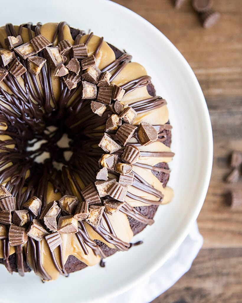 An above view of a chocolate and peanut butter bundt cake topped with reeses peanut butter cups on a white plate.