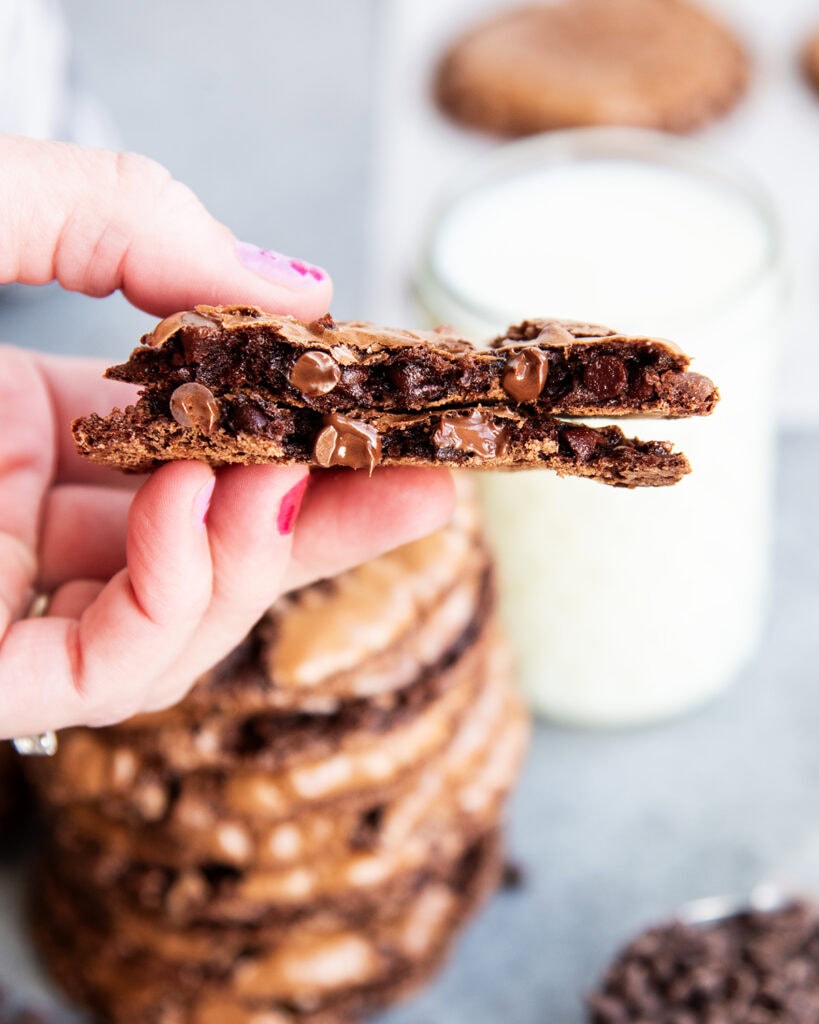 A hand holding two halves of a flourless chocolate brownie cookie showing the melty chocolate inside.