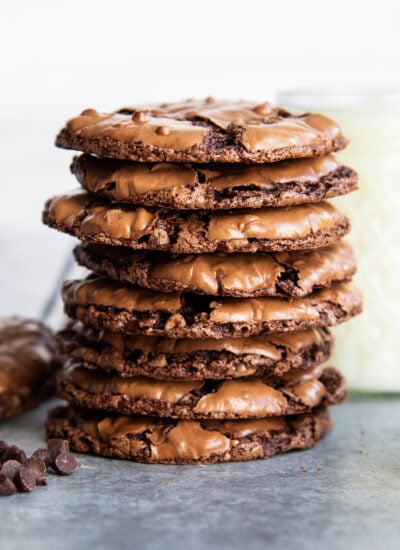 A stack of thin and chewy flourless chocolate cookies next to a cup of milk.